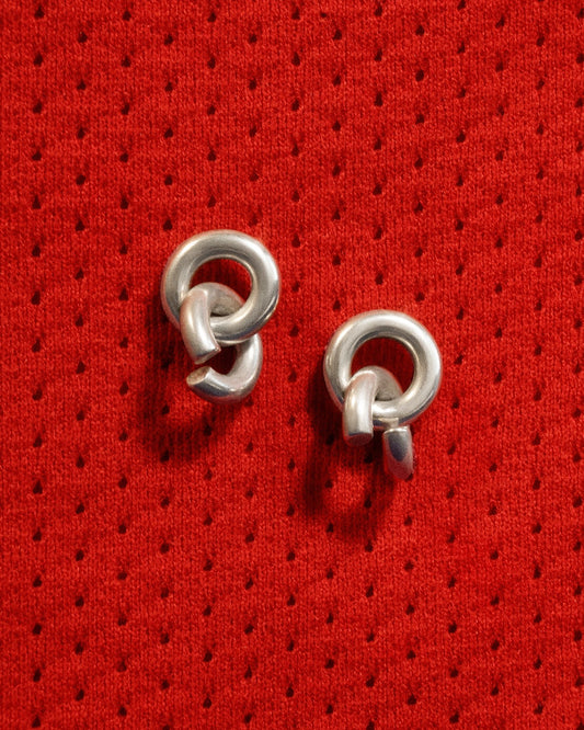 Heavy silver chain earrings with two links laying on bright red fabric with small pin holes