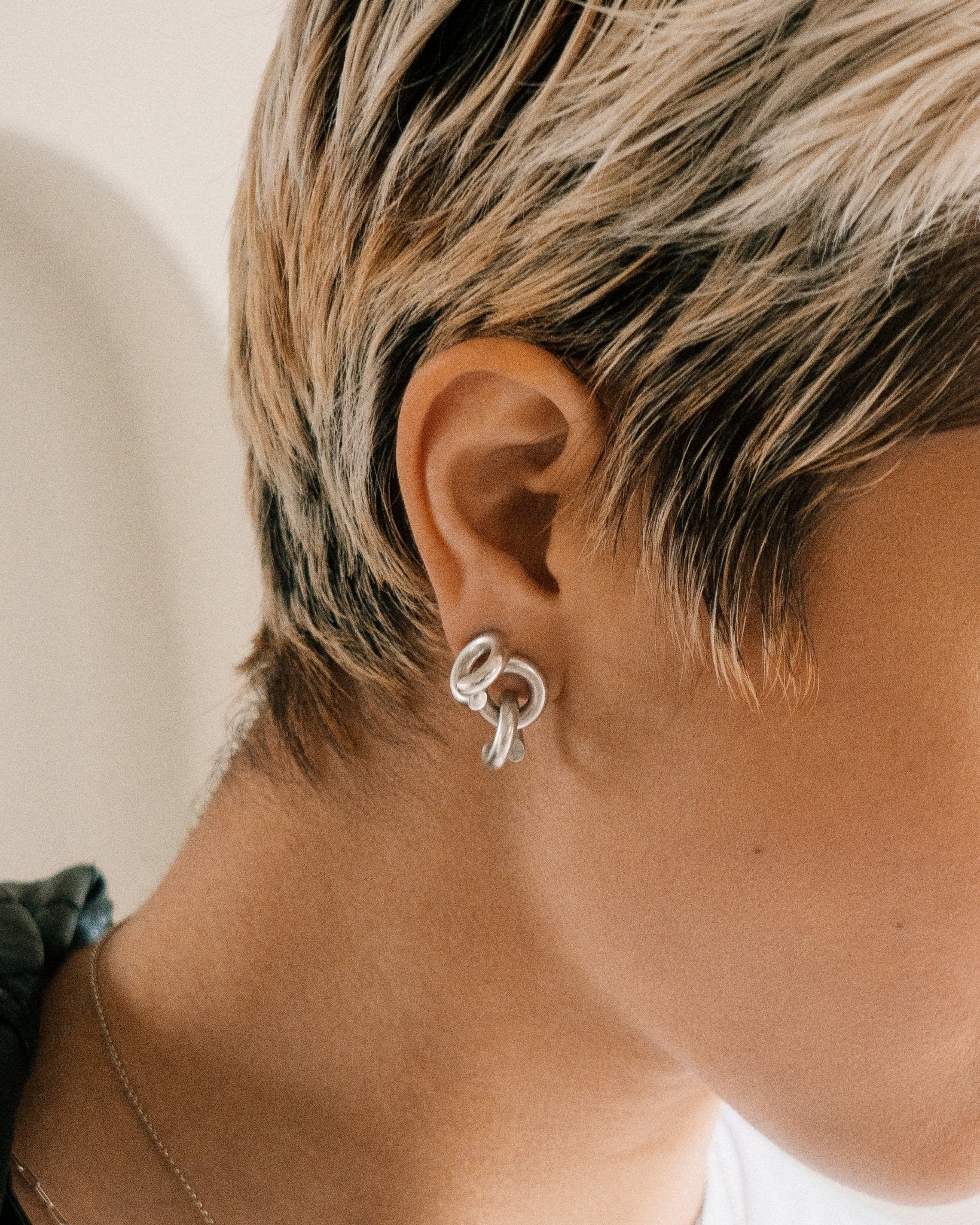 right side of woman's face with heavy silver chain earrings in lower earlobe piercing and silver loop earring in top piercing 